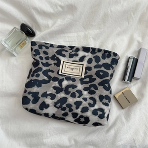 Dettaglio della borsa trucco leopardata con etichetta Pleasant Time su tessuto bianco