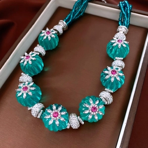 Vue détaillée du collier de perles vertes avec pendentifs floraux et pierres rouges en boîte