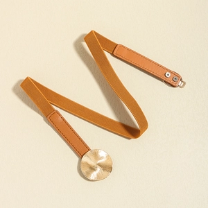Detail of caramel elastic waist belt featuring a textured golden metal circular buckle