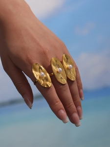 Detail of finger wearing gold plated shell pearl rings against a beach background