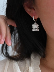 Detailed view of silver bell-shaped drop earrings with shiny zircon and white pearls