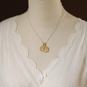 Detail of vintage gold sun and angel pendant necklace on model with small pearls