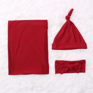 Three-piece newborn set with dark red swaddle blanket, knot hat and bow headband on white rug