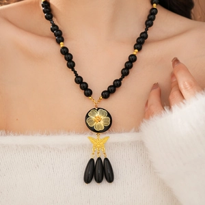 Detail of vintage beaded necklace featuring gold flower pattern and butterfly drop tassel