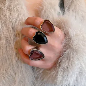Three zircon heart-shaped open rings in purple, black, and amber worn on hand