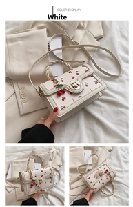 Detailed view of white cherry print handbag with floral metal lock and braided handle