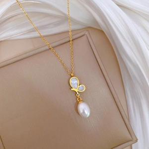 Golden butterfly necklace with white shell inlay and pearl drop on silk background