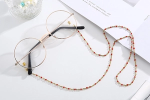 Detail of gold chain mask holder with red beads on a white minimalist background