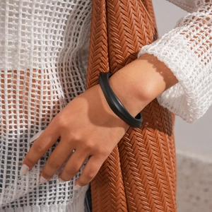 Close-up of minimalist black matte acrylic bangle on wrist with woven texture background