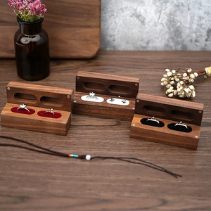 Three walnut wood ring boxes with red, white and black velvet linings on a wooden table