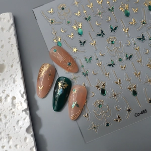 Macro detail of gold butterfly nail stickers with star and moon patterns on dark green nails