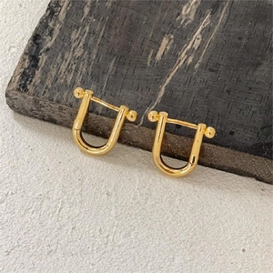 Close-up of golden U-shape horseshoe link earrings with polished metallic finish