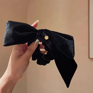 Detailed view of a black velvet bow scrunchie featuring a small gold logo charm