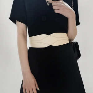 Detail of cream elastic waist belt with criss-cross design over a black dress