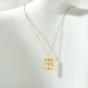 Close-up of gold tarot pendant with snake motif and zircon accents on white bust