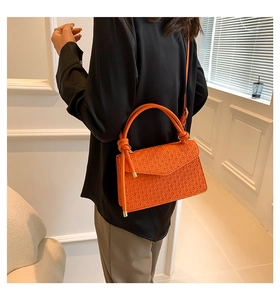 Detail of orange woven crossbody bag with decorative knot and slim leather strap