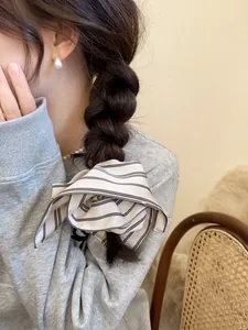 Detail of striped silk scrunchie worn on a braid with elegant pearl earring accessory