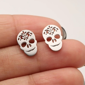 Close-up of gothic skull stud earrings in silver finish held between fingers for size