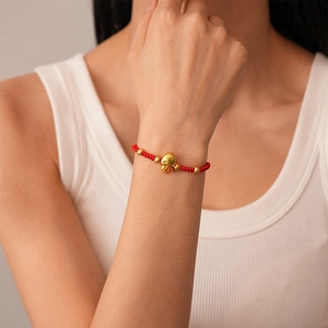 Close-up of red braided rope bracelet with golden lucky charm and beads on wrist