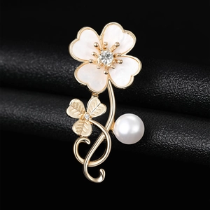 Detailed view of a gold clover brooch with white shell petals, crystal, and a large pearl