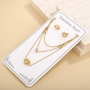 Detail of gold stainless steel necklace and earrings set with eye motifs on textured stone