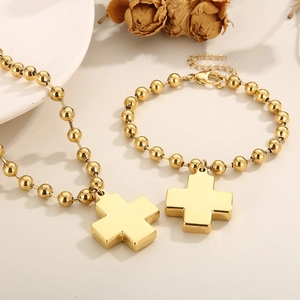 Polished gold beaded necklace and bracelet set with minimalist cross pendants on a tray