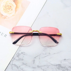 Rimless sunglasses with pink gradient lenses and gold metal frames on marble background