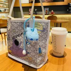 Space-themed tote bag with astronaut patterns and a blue silicone charm in a cafe setting