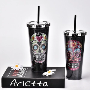 Close-up of black plastic tumblers with rhinestone skull patterns and silver lids