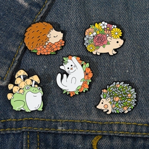 Set of five enamel pins featuring cute hedgehog, cat and frog on denim fabric background