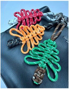 Détail de trois breloques sapin de Noël tissées en rouge, orange et vert sur un sac noir