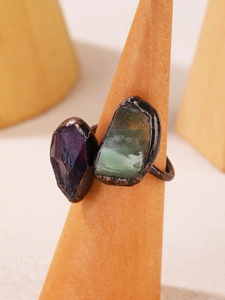 Detailed close-up of a bronze ring set with natural raw purple and green crystals
