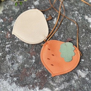Detail of acorn-shaped mini leather cross-body bags in beige and orange on stone