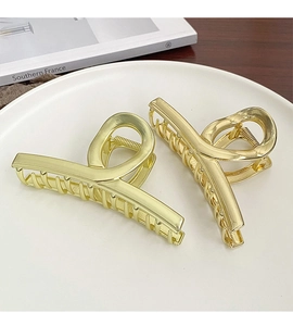 Macro detail of two large golden twisted metal hair claws on a minimalist white tray