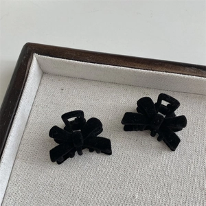 Close-up of two mini black velvet bow hair clips on a minimalist linen tray display