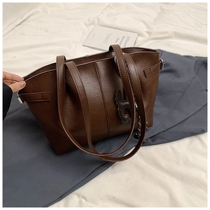 Detail of dark brown tote bag texture and cat charm on white wrinkled sheets