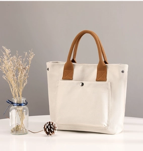 Canvas tote bag detail, featuring brown handles and front pocket with snap button.