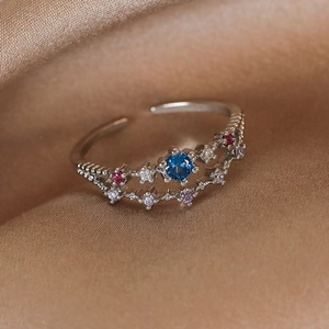 Detailed close-up of a crown-shaped silver ring with colorful zircons on champagne silk