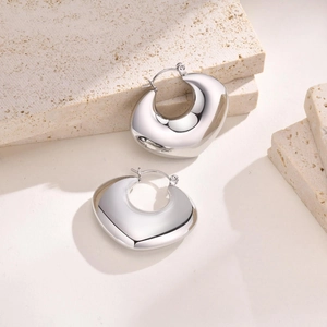Macro shot of silver chunky hollow hoop earrings on a natural stone textured background