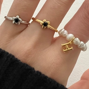 Detail of stacked S925 silver flower rings and pearl band with a gold H letter charm