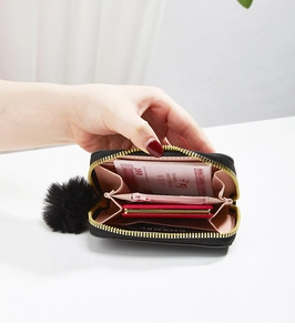 Detail of black wallet showing pink interior with card slots and a pom-pom charm