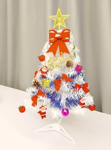 Mini white Christmas tree with blue tinsel, red bows, and festive ornaments on base