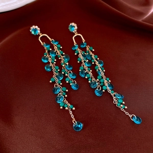 Detail of teal beaded tassel earrings with gold chains and crystals on silk background
