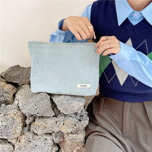 Close-up of a blue corduroy makeup bag held by a model against natural rock background
