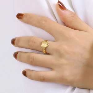 Gros plan d'une bague coeur dorée avec texture martelée sur la main et tissu blanc