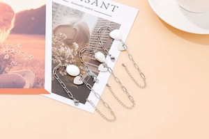 Détail de bracelets cœur argentés avec perles et fermoir mousqueton sur un magazine