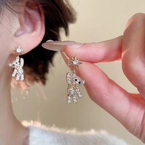 Detailed view of gold bear earrings with pavé crystals and star studs on ear