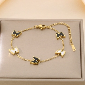 Detailed shot of golden butterfly bracelet with black and white shell pendants and lobster clasp