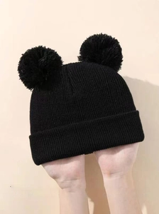 Close-up of black knit hat with double pom-poms showing thick texture and elastic cuff