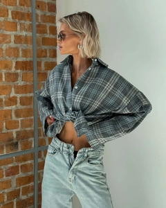 Blue-gray plaid long sleeve shirt paired with light blue jeans on vintage brick background